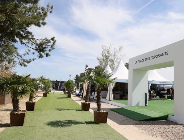 Stand DSP Allée verdoyante avec des palmiers et des tentes blanches sous un ciel bleu.